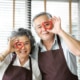 Asian senior couple wear brown aprons are holding red cookies cutters in heart shape over their eyes