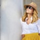 middle aged woman wearing sunglasses and straw hat while standing at balcony