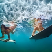 Two women surfing and diving beneath the waves, in danger of getting Surfer's Eye or Pterygium.