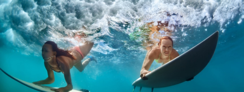 Two women surfing and diving beneath the waves, in danger of getting Surfer's Eye or Pterygium.