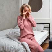 Woman sitting up in bed and rubbing at her eyes, dealing with blurry vision after waking up.