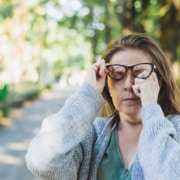 Older woman rubbing at her eye, possibly due to a recurring pterygium after eye treatment.