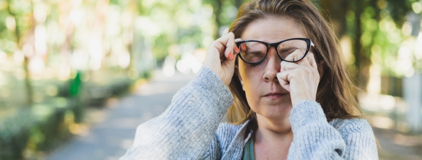Older woman rubbing at her eye, possibly due to a recurring pterygium after eye treatment.